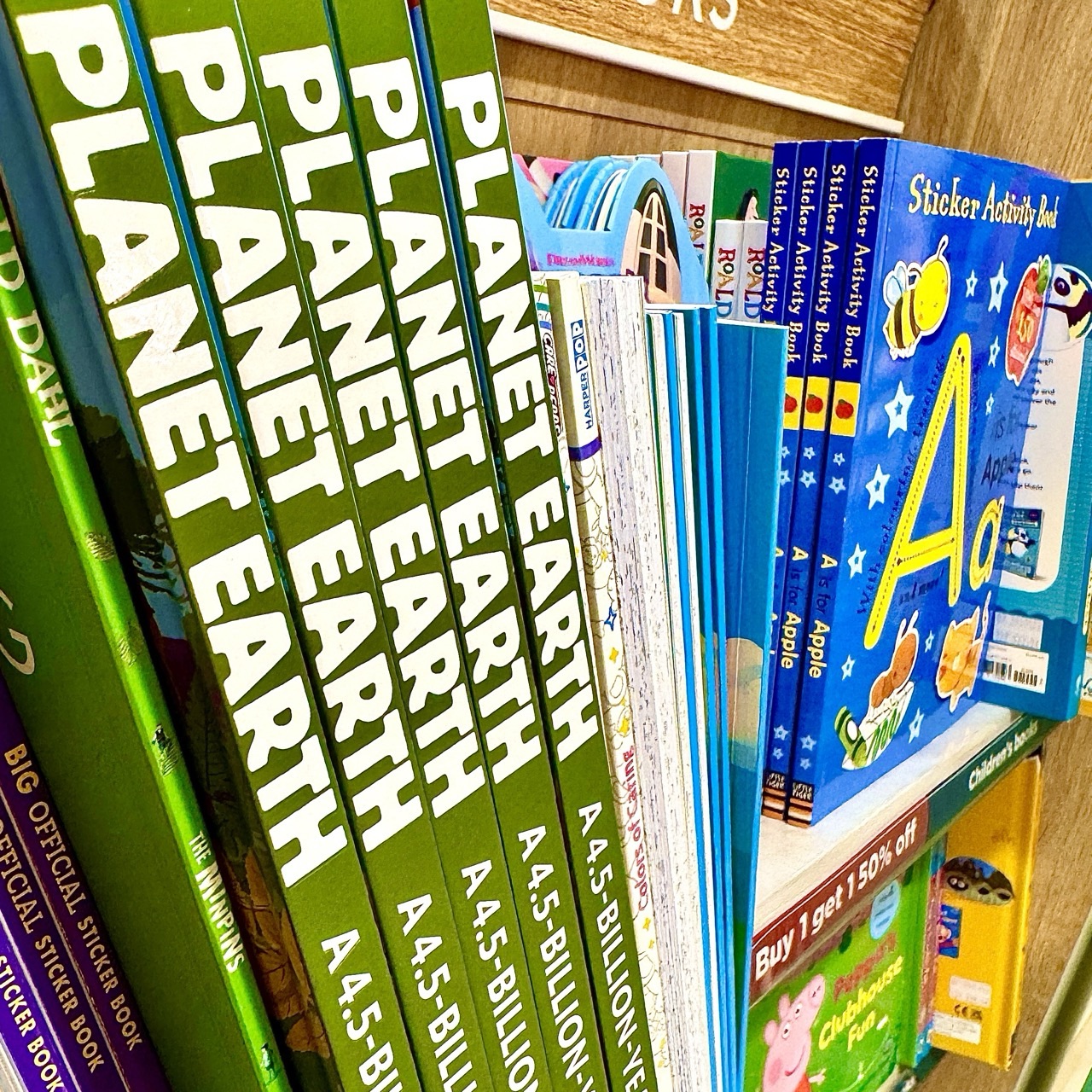 Large reference books about Planet Earth stand upright on a shelf beside other illustrated educational titles.