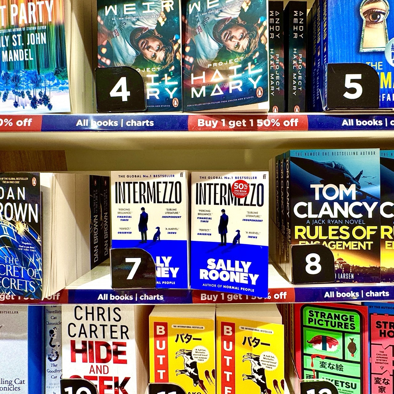 Rows of novels are displayed with their covers facing out, alongside numbered shelf markers in a bookshop.