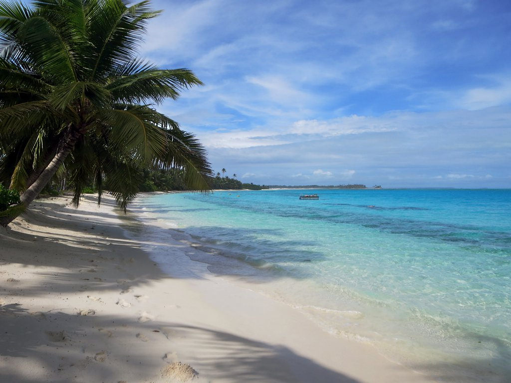 Turquoise reef lagoon water and a white sandy beach lined with coconut palms on Direction Island, Cocos (Keeling) Islands.