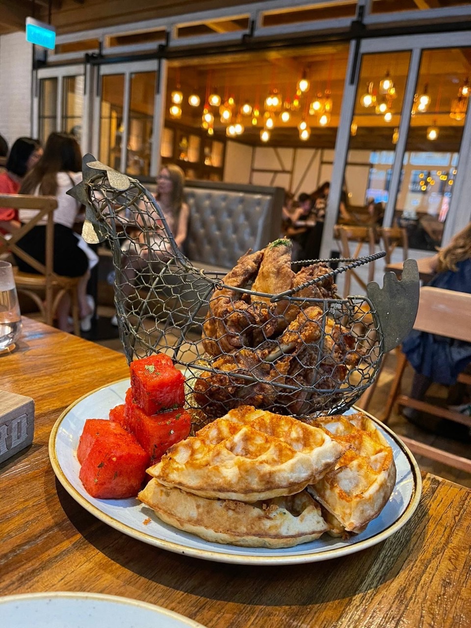 Chicken and waffles served with watermelon cubes inside a café.