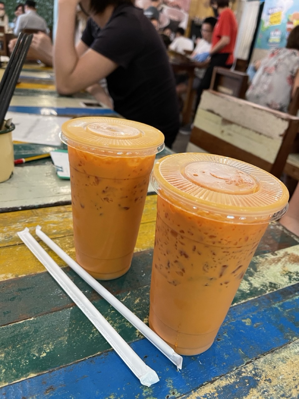 Iced Thai milk tea served in clear plastic cups with straws inside a Thai restaurant.