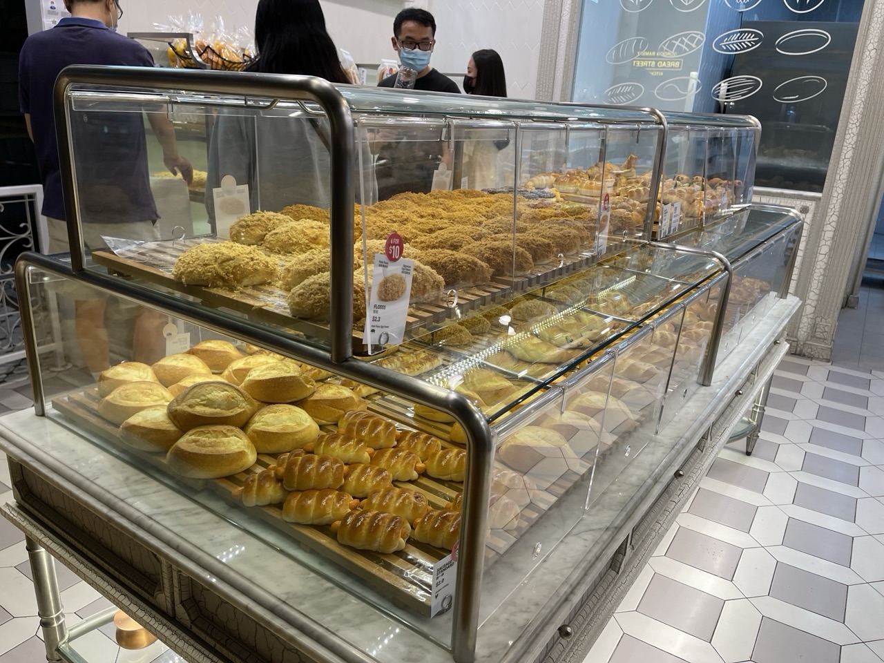 Bread and confectionery displayed in bakery cases with customers choosing items.