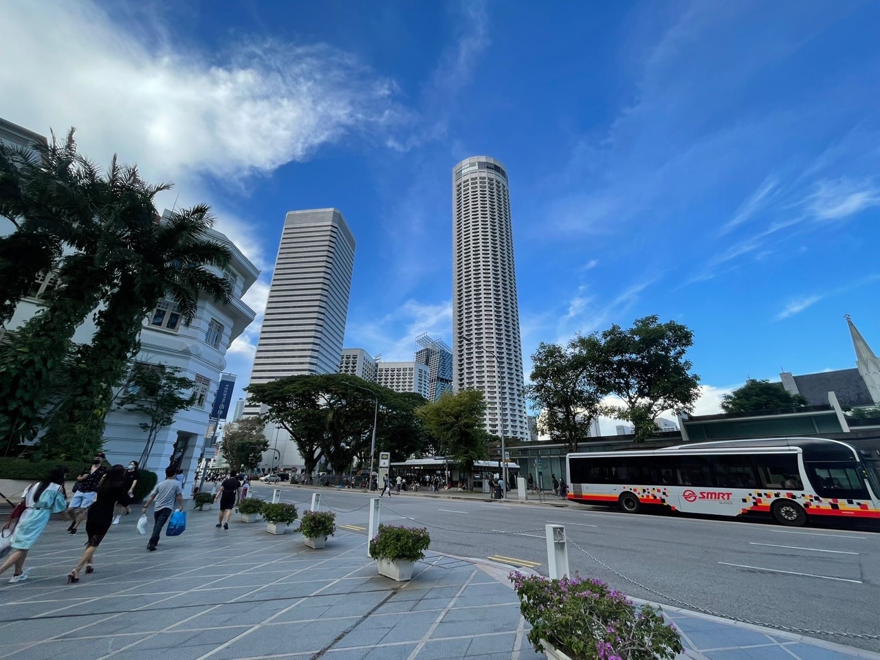 Raffles City Shopping Centre exterior with a bus, road traffic and shoppers in Singapore.