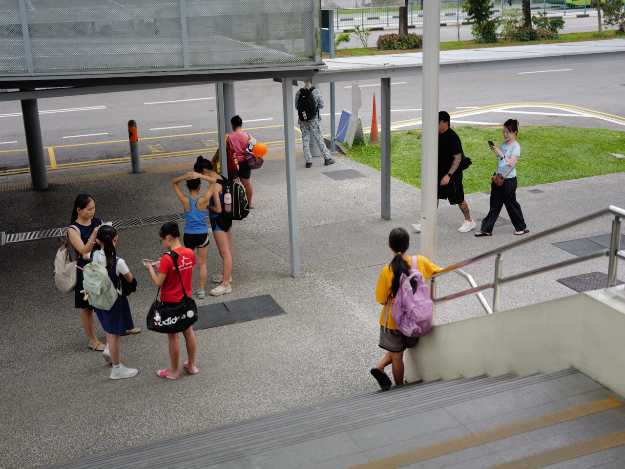 Families and other passengers waiting at a bus stop on Upper Bukit Timah Road.