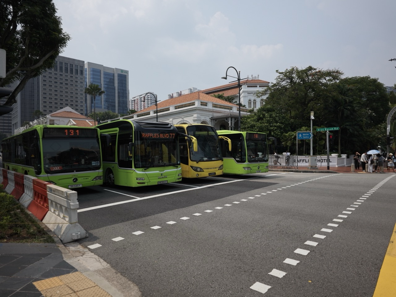 Four buses stopped at a red light near Raffles City and Raffles Hotel Singapore.