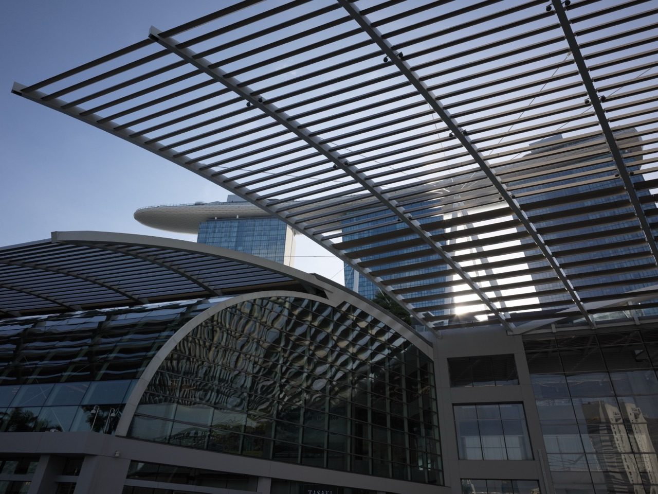 Waterfront promenade outside The Shoppes at Marina Bay Sands with roof architecture and the hotel towers and SkyPark behind