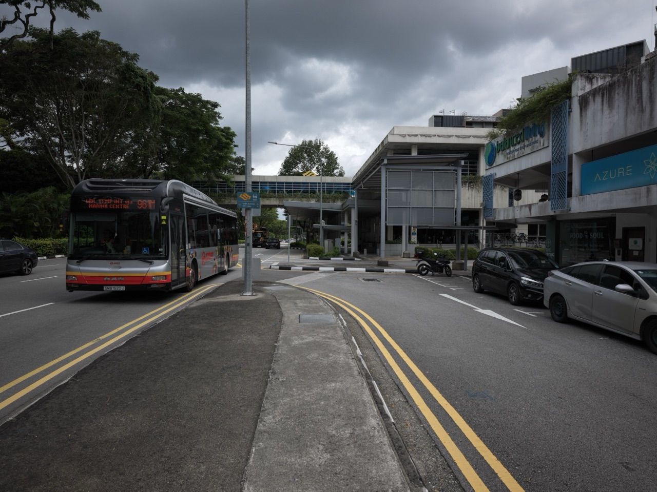 Public bus on Bukit Timah Road beside shophouses, the Sixth Avenue MRT entrance and a pedestrian overhead bridge
