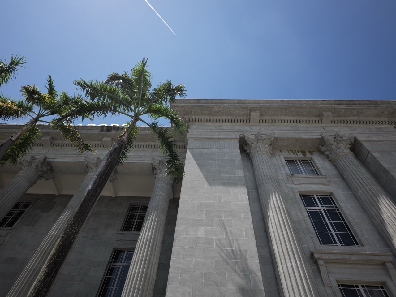 National Gallery Singapore with palm trees in the foreground and an aircraft contrail in the sky