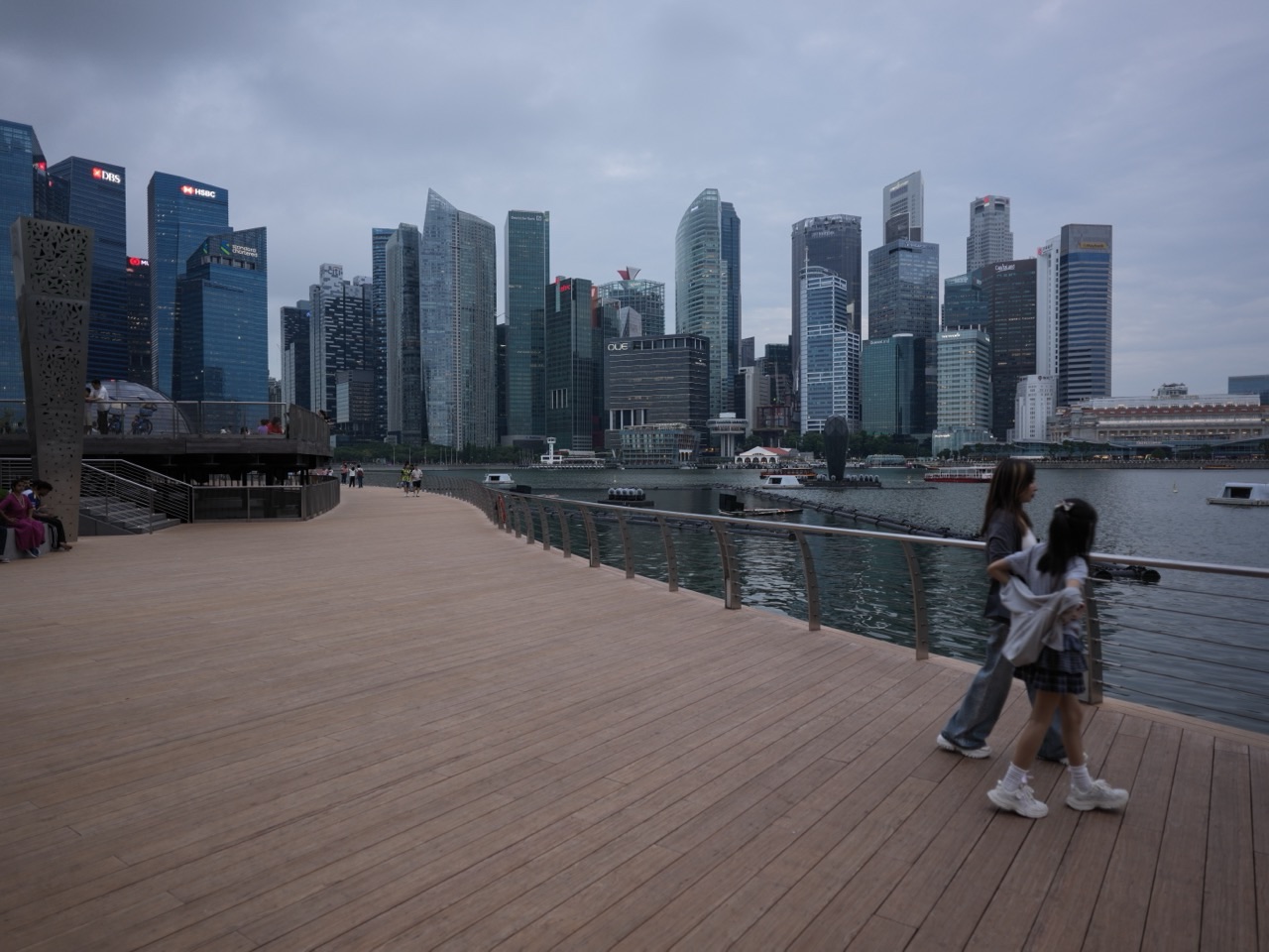 Family and visitors walking along the Marina Bay waterfront with the financial district and The Sail in the background