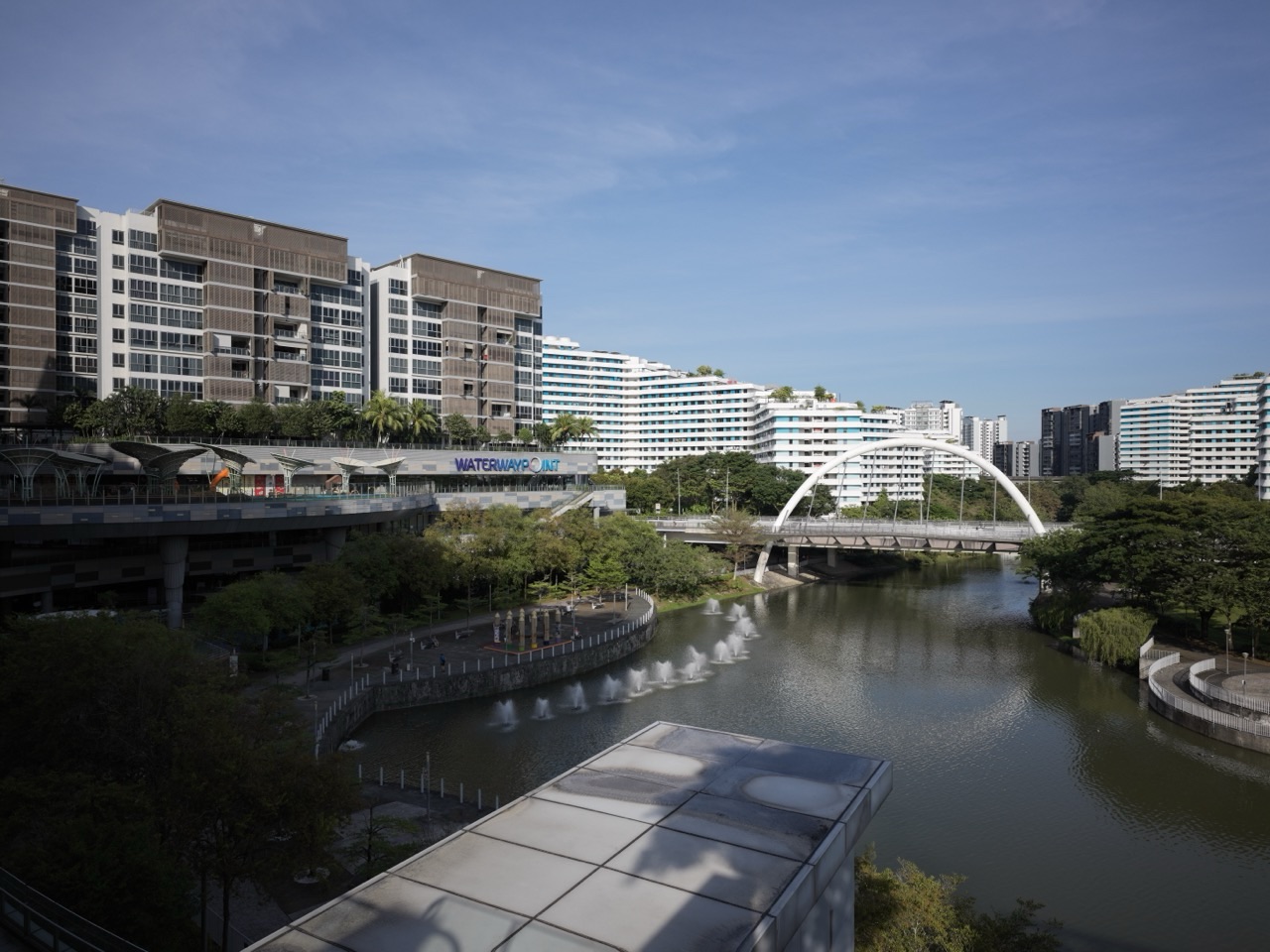 Waterway Point and Watertown condominium beside Punggol Waterway Park, with the Arc Bridge and HDB blocks in view.