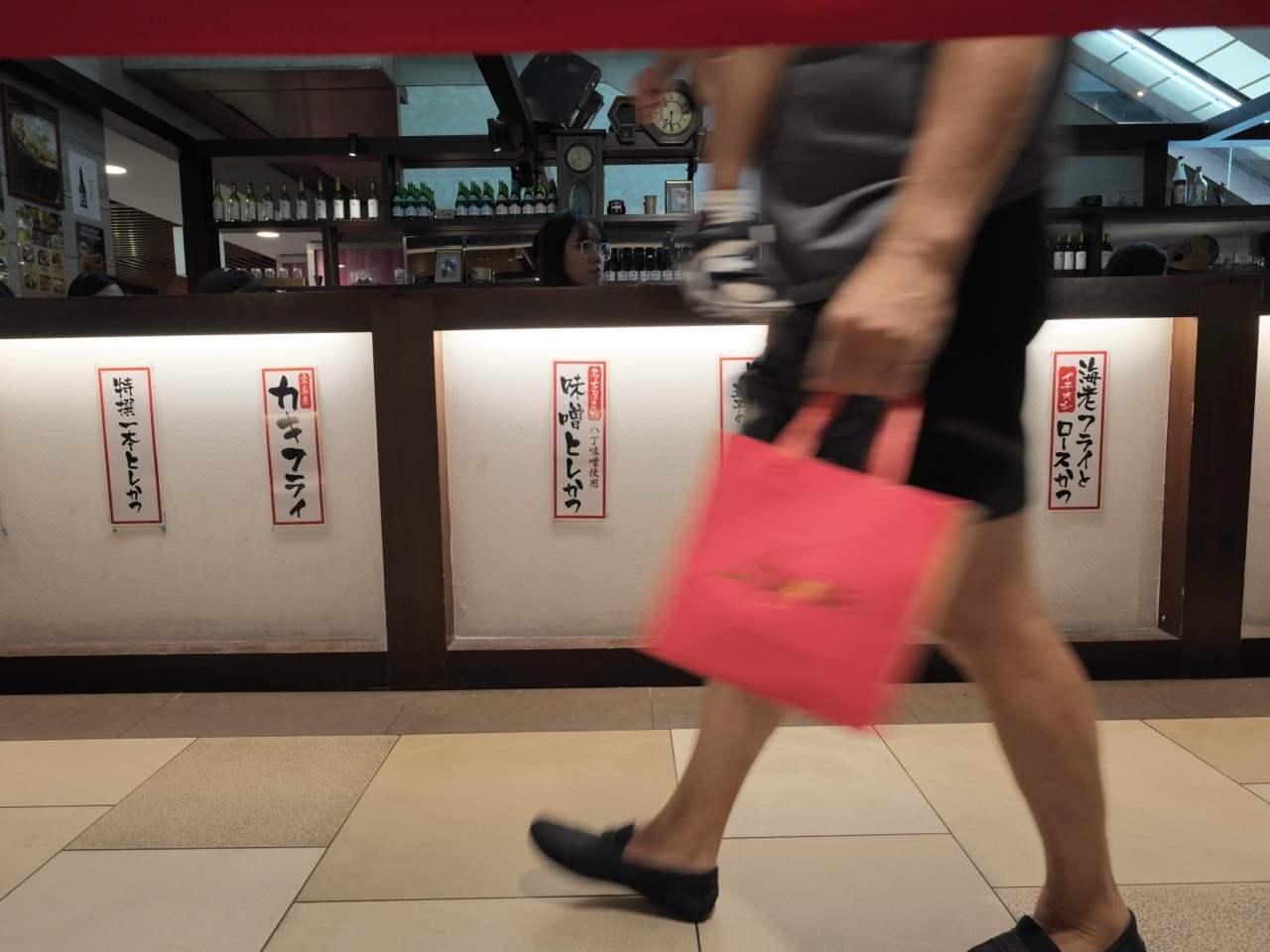 Adult carrying a baby and a shopping bag while walking past a Japanese restaurant in Singapore.