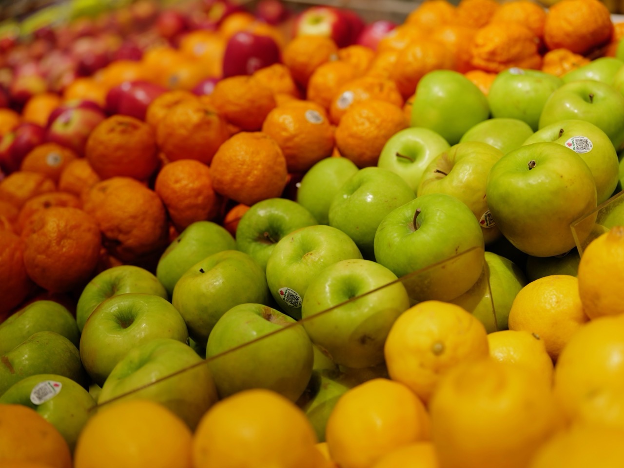 Green apples and oranges displayed in a supermarket produce section.
