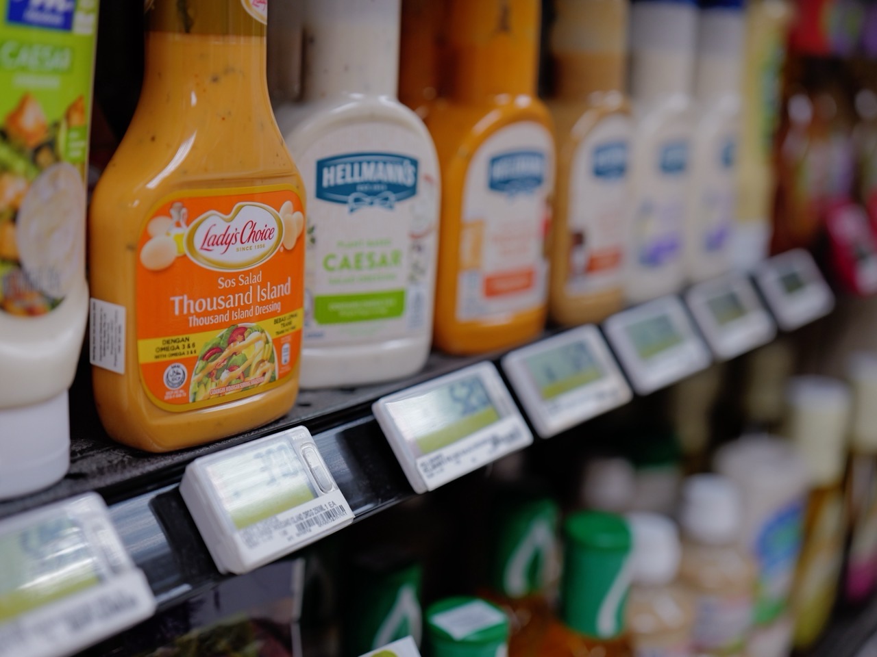 Bottles of salad dressing displayed on a supermarket shelf with visible prices.