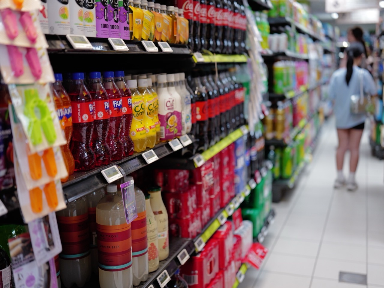 Shoppers browsing soft drinks displayed in a supermarket aisle.