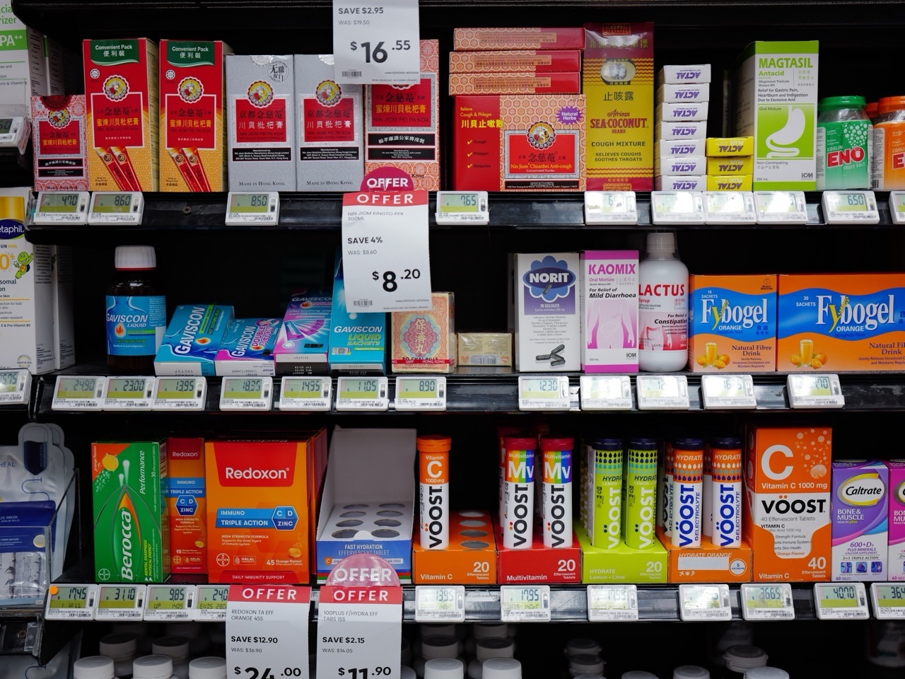 Vitamins and health products displayed with price labels and promotional offers in a supermarket.