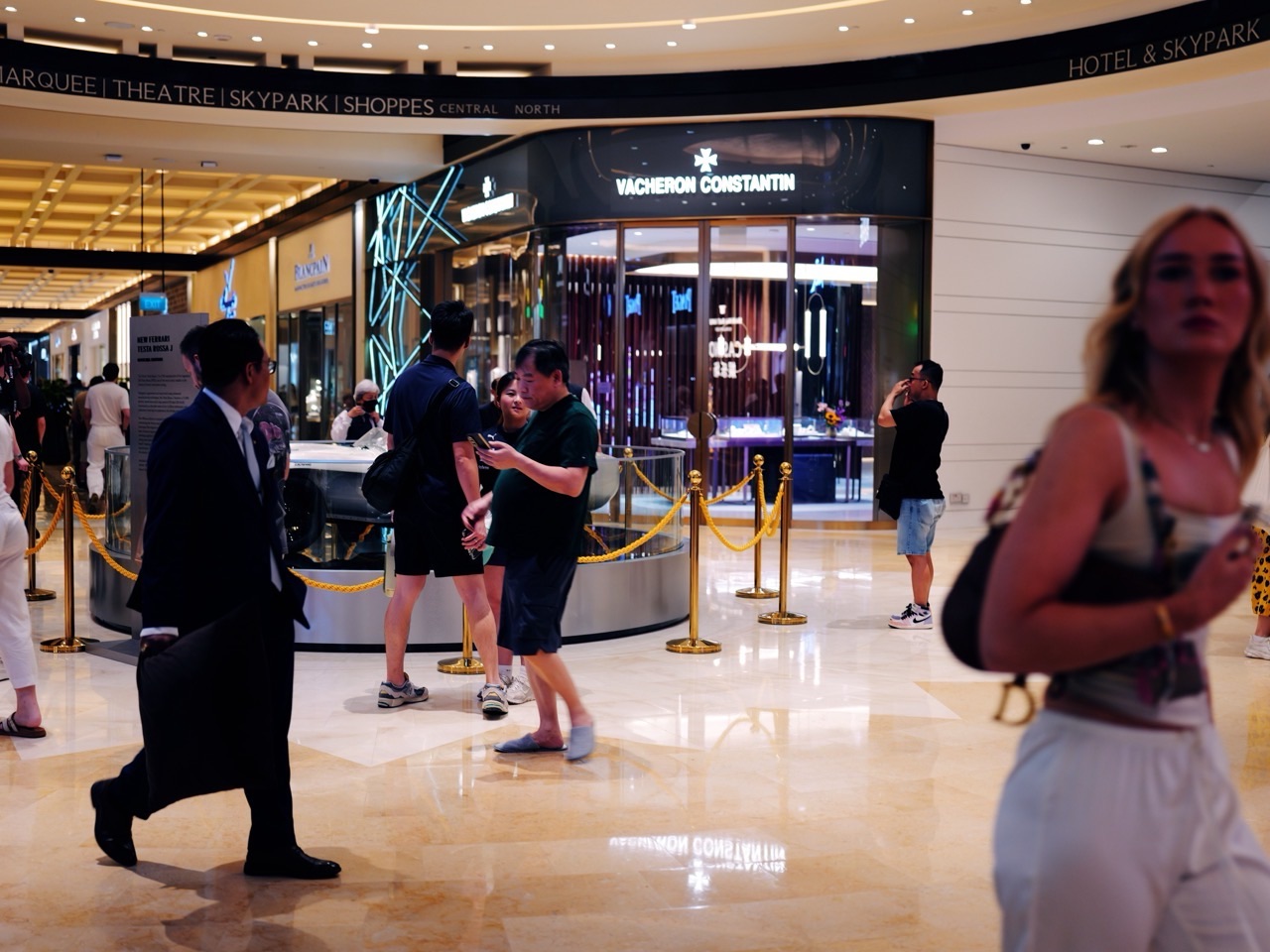 A blurred visitor moving through a Marina Bay Sands foyer with shoppers and a car display behind.