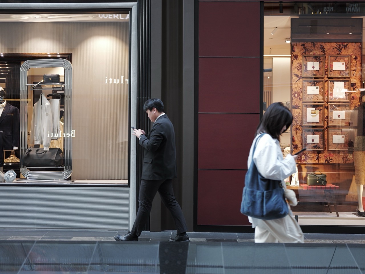 Two visitors in front of stores at Marina Bay Sands, with the visitor on the right looking at a phone.
