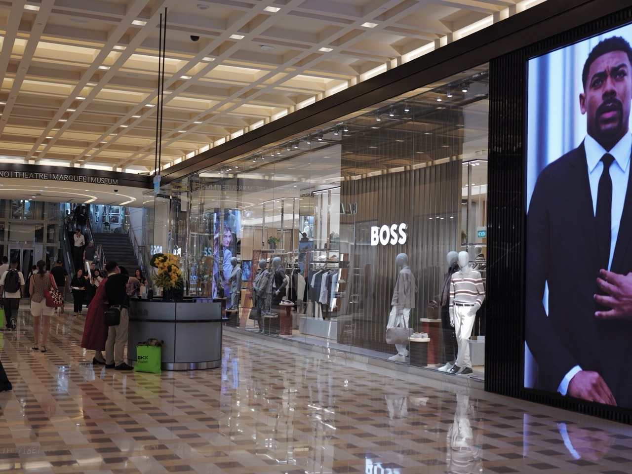 A menswear storefront beside a concierge desk where shoppers ask questions at Marina Bay Sands.