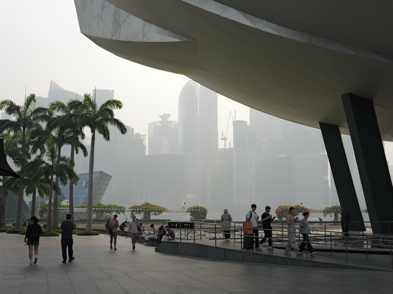 Pedestrians with a hazy Singapore skyline beyond and ArtScience Museum on the right at Marina Bay Sands.