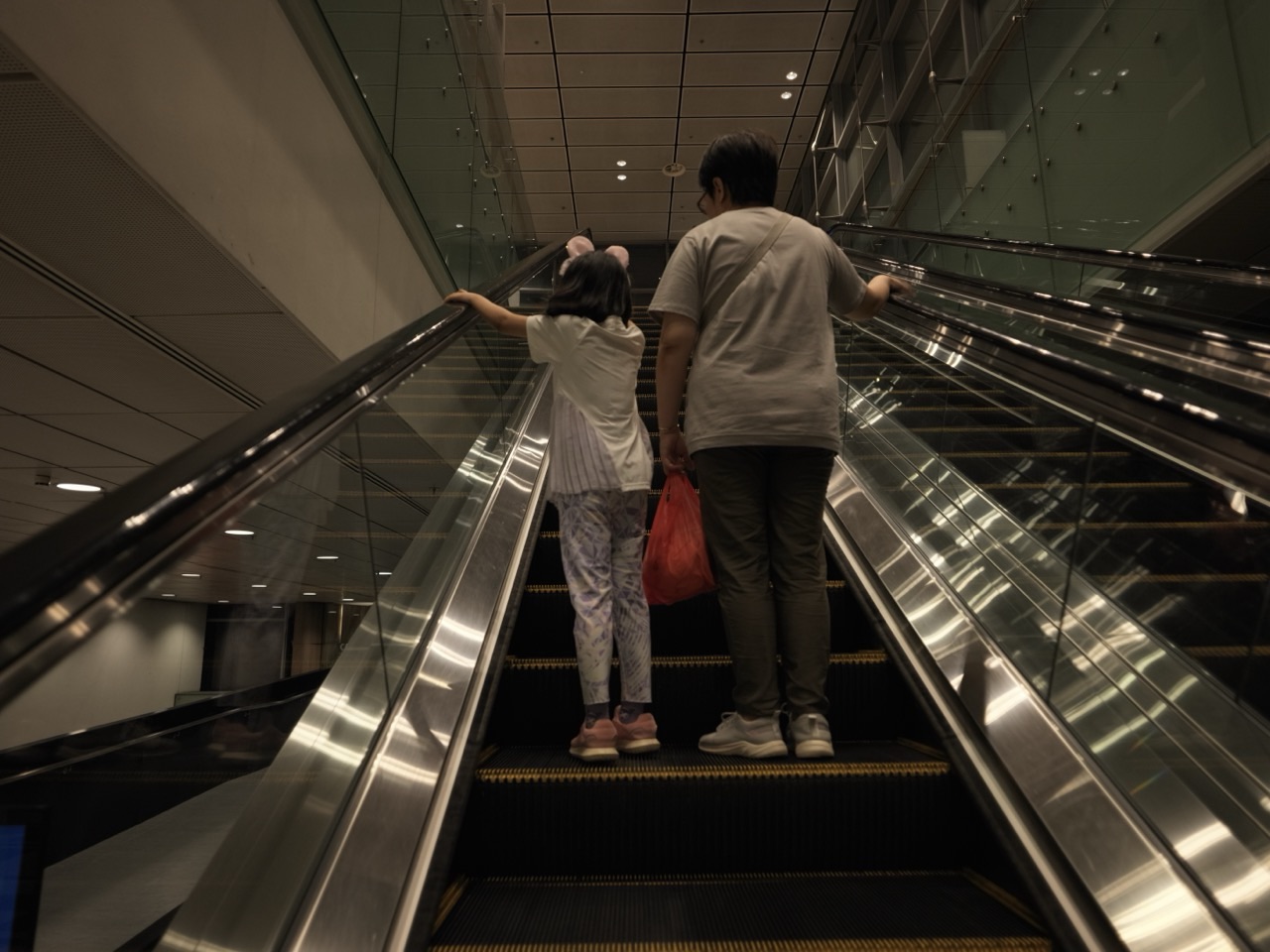 Adult and child riding an escalator at Singapore Changi Airport.