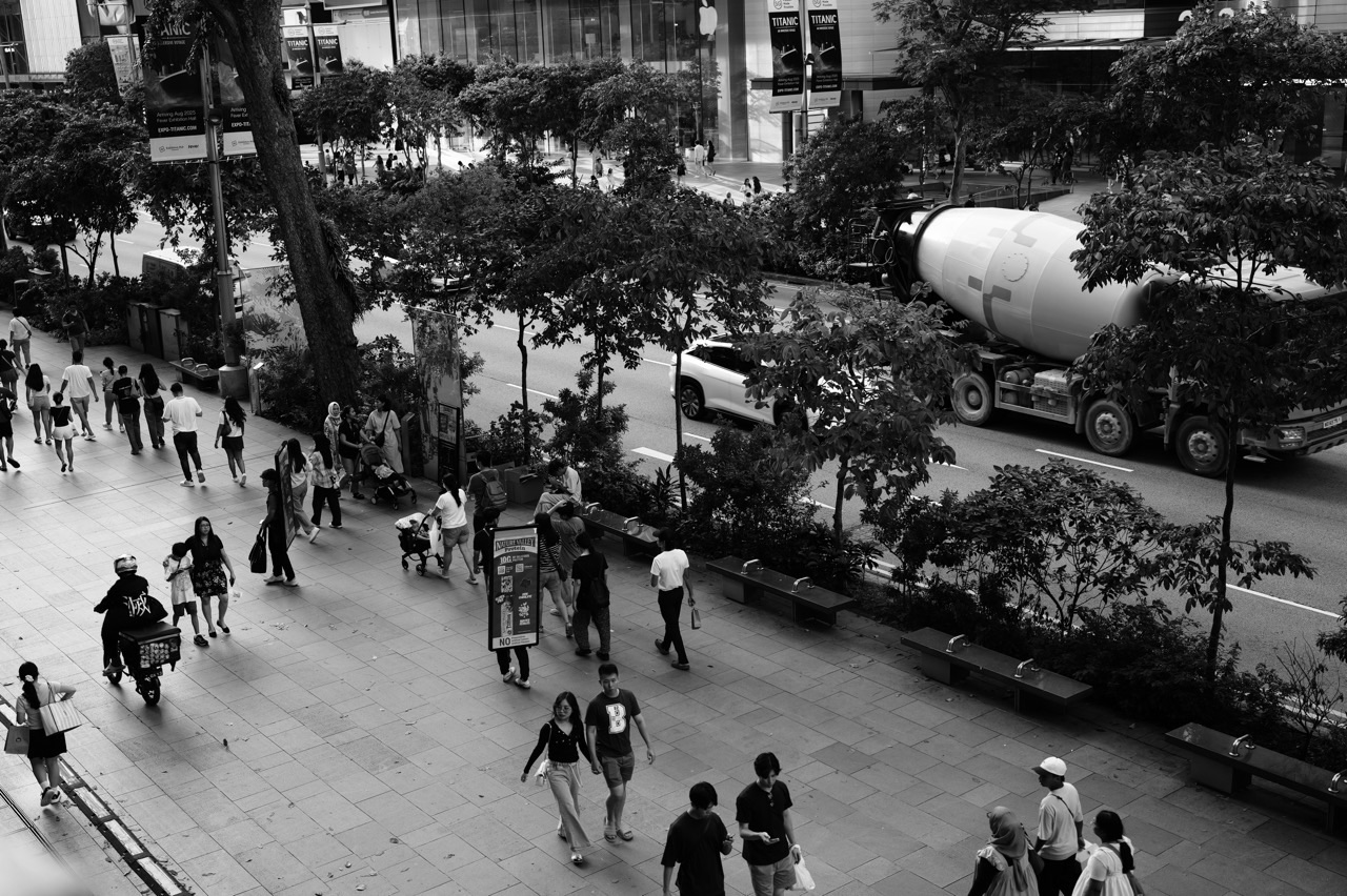 Pedestrian walkway beside Orchard Road traffic including cars and a cement mixer in Singapore.