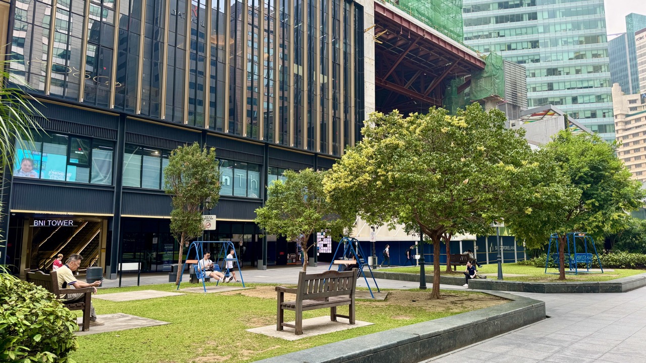 People seated in Raffles Place Park while a man walks out of the nearby MRT station.