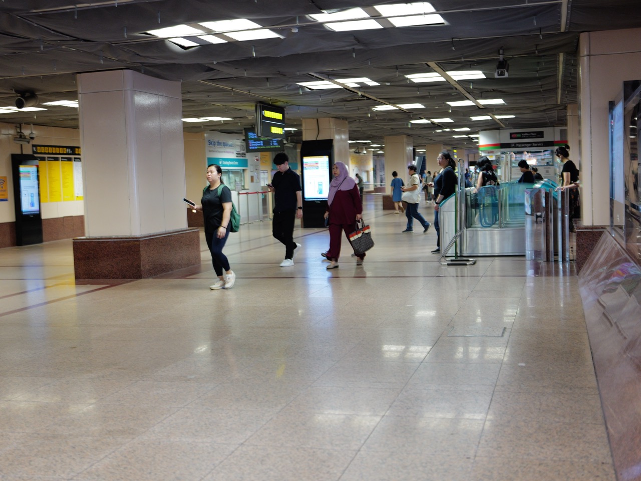 Commuters walking through fare gates at Raffles Place MRT with passenger-service facilities behind.