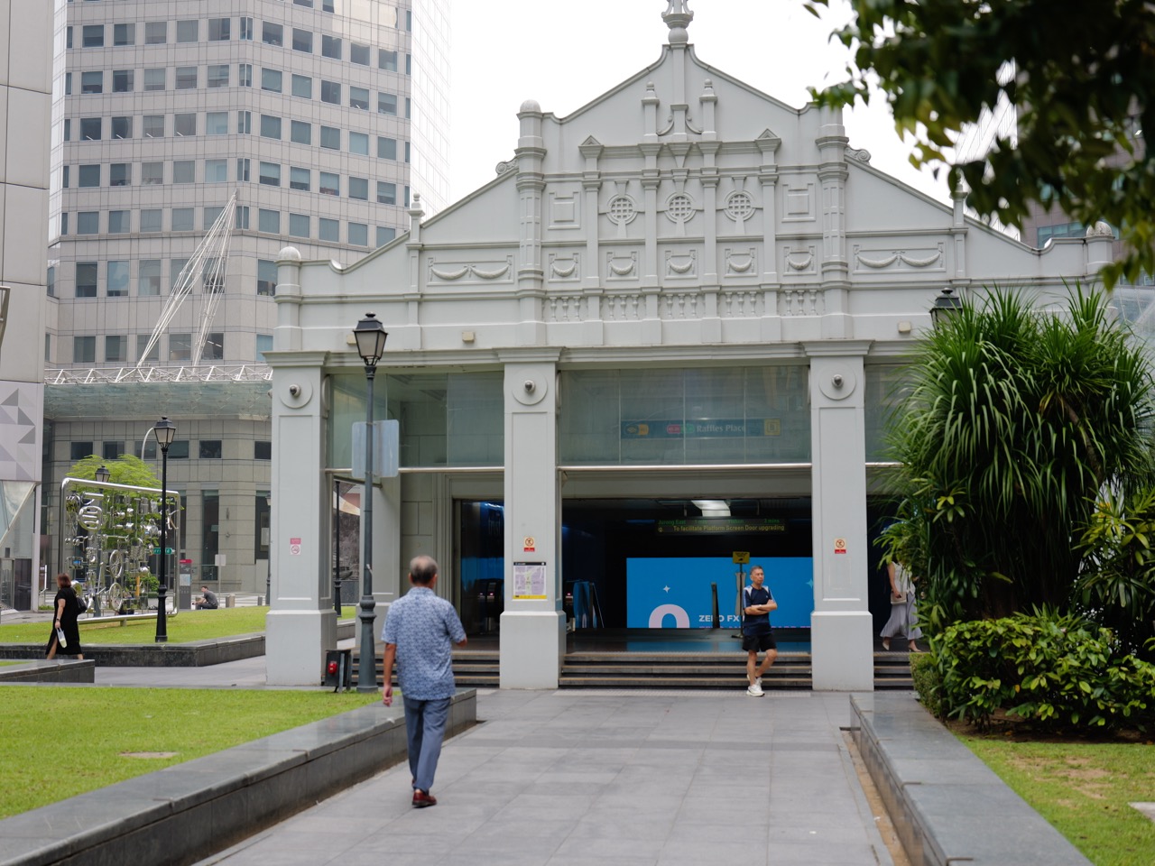 People entering and leaving Raffles Place MRT station at its ground-level entrance.