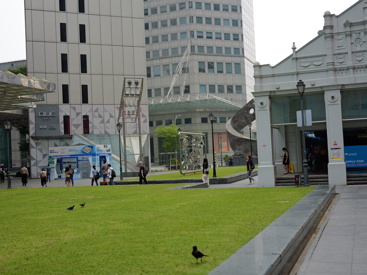 Office workers leaving Raffles Place MRT near UOB and OUE buildings and a public art installation.