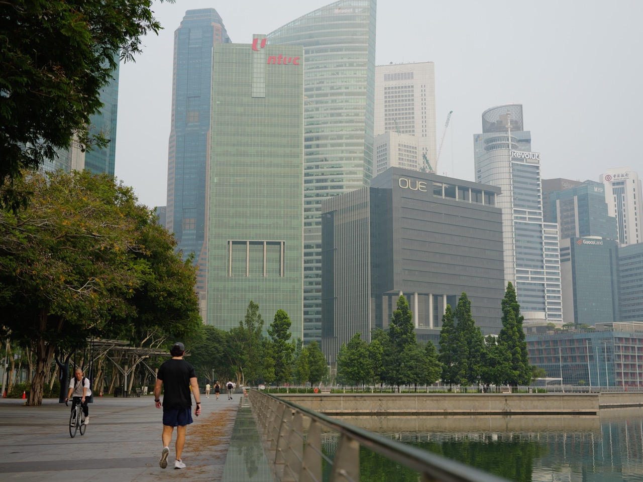 Cyclist and man walking near the Shenton Way financial district skyline in Singapore.