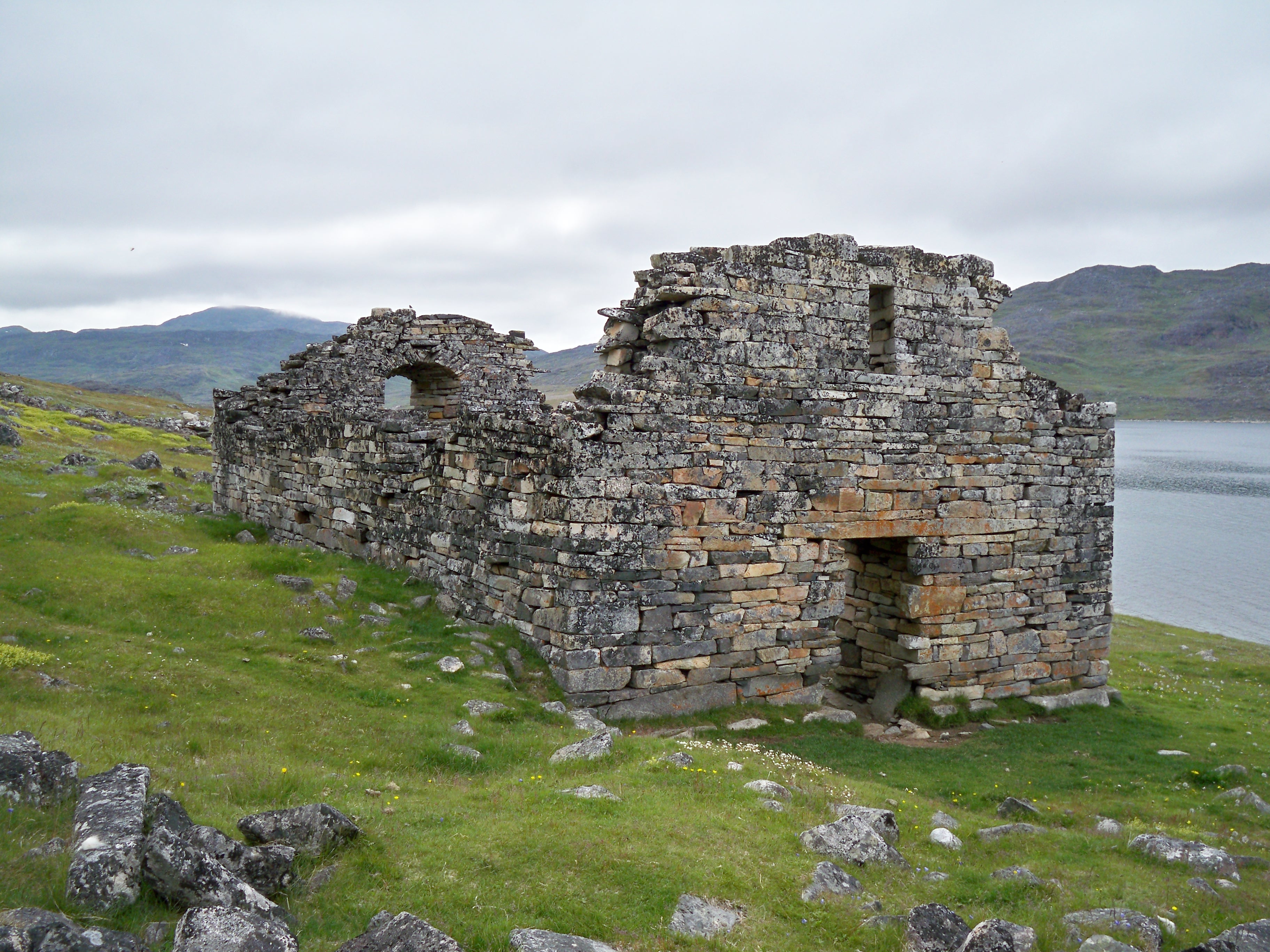 Actual surviving stone walls of the medieval Norse church at Hvalsey in southern Greenland, with a green fjord landscape behind.