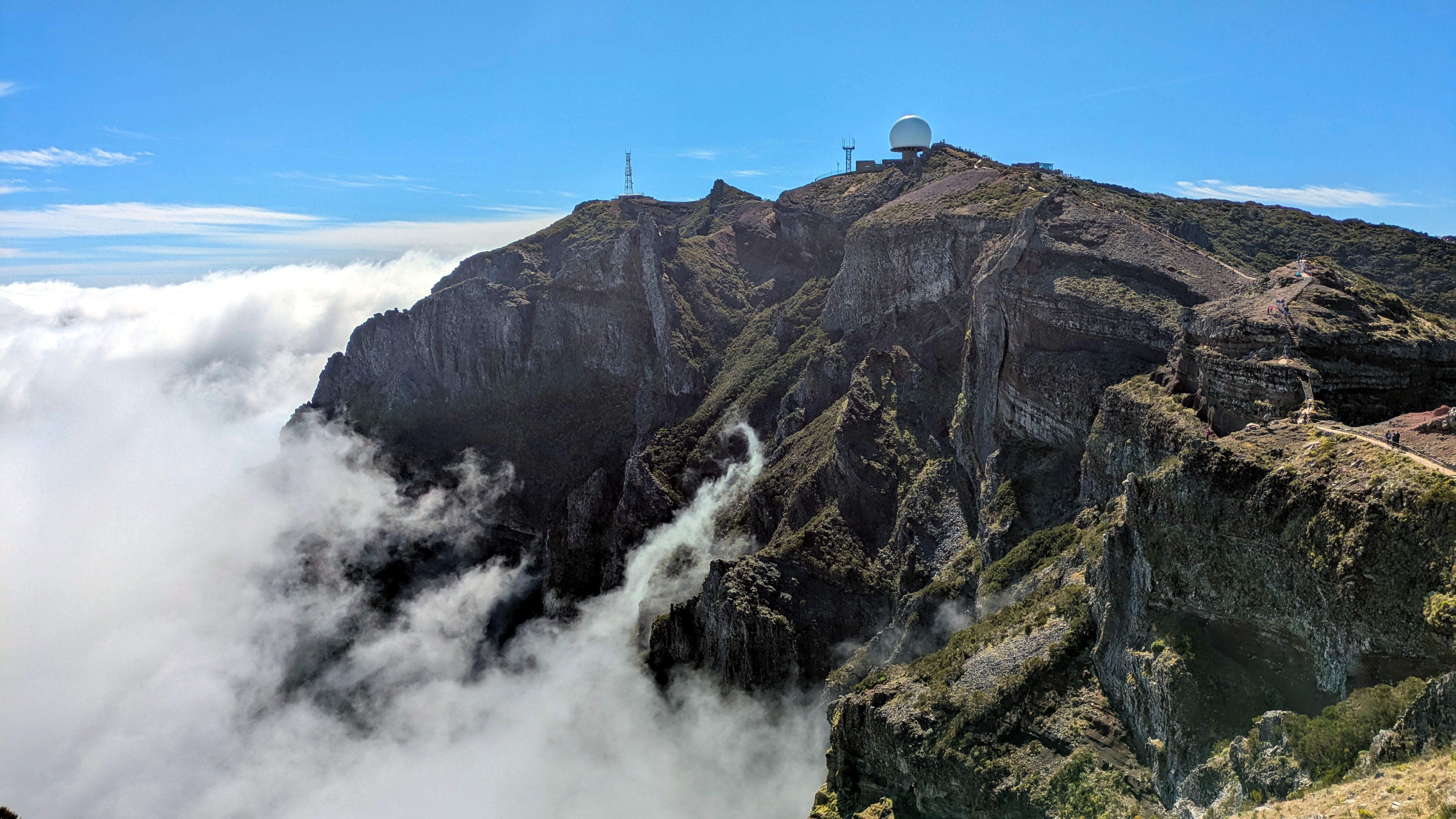 Pico do Areeiro rocky mountain summit on Madeira rises above a bank of clouds, with a radar dome visible in the distance.