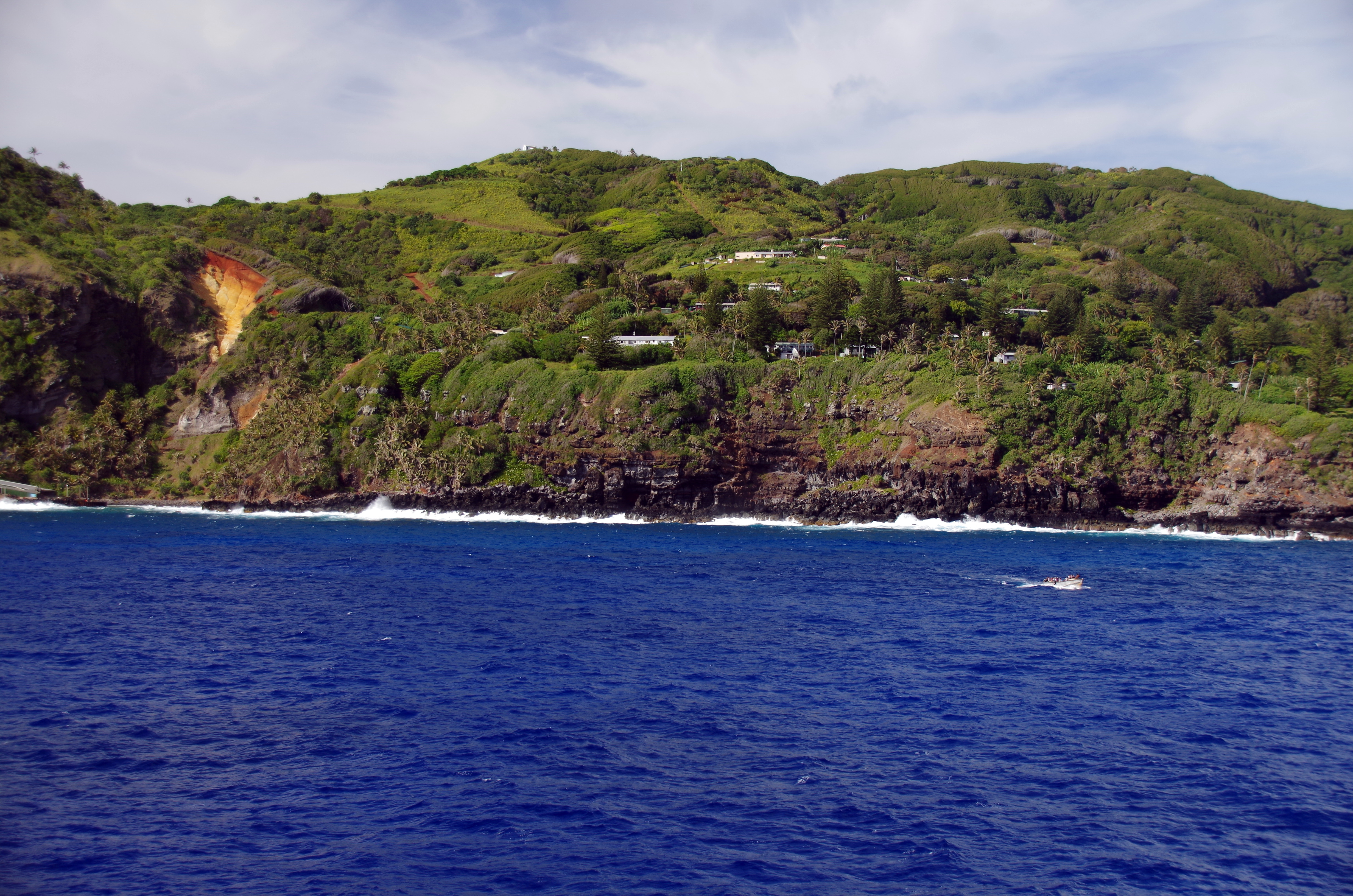 View from the sea across steep green volcanic cliffs to scattered houses of Adamstown, Pitcairn Island, photographed in December 2017.