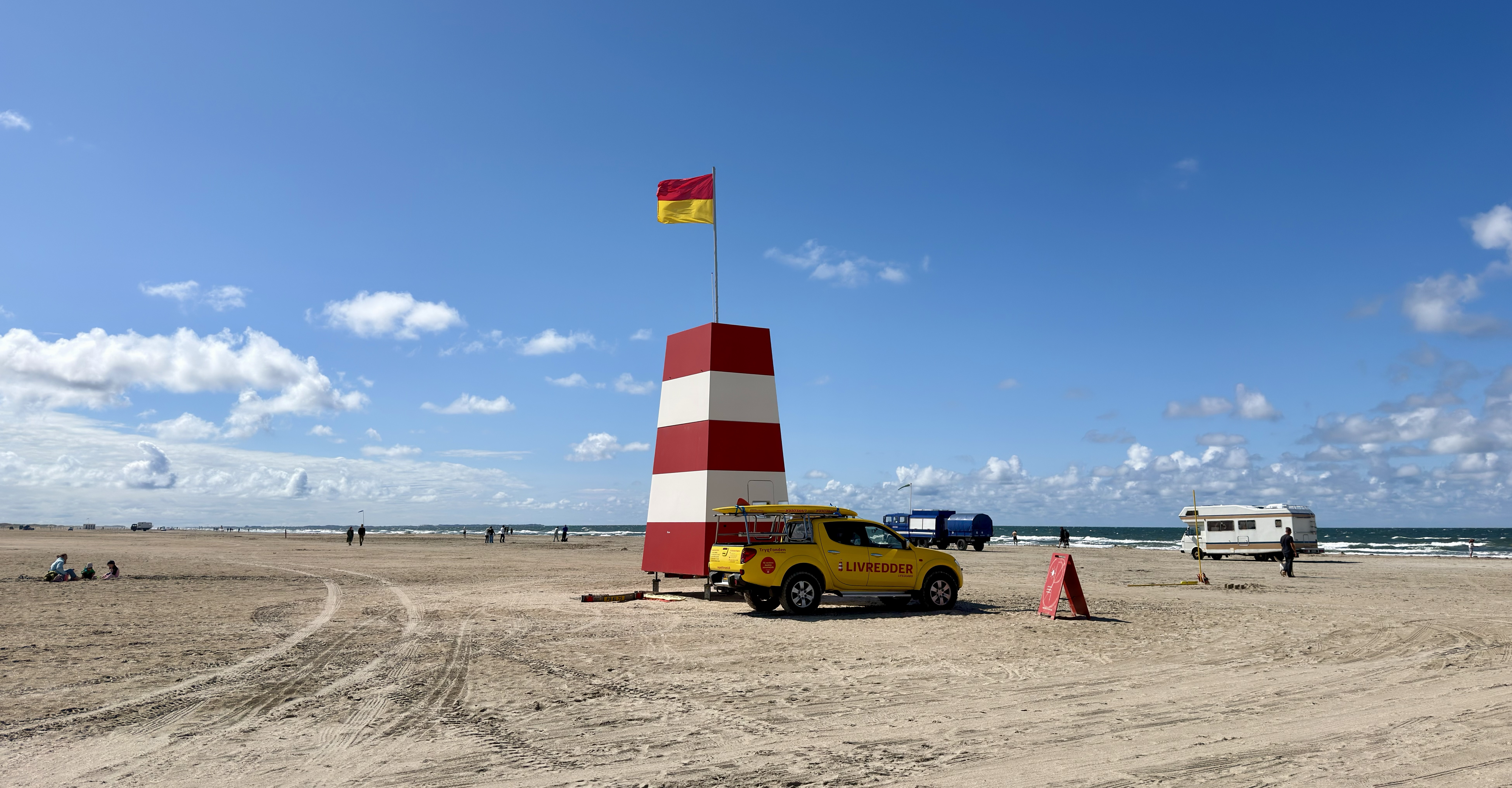 Red and white lifeguard marker with a yellow rescue vehicle on the broad sandy Lakolk Strand beach on Rømø in Denmark