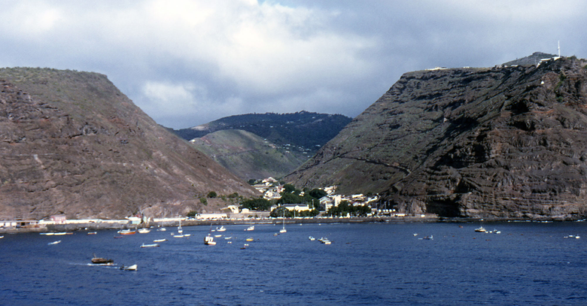 Archival coastal panorama of Jamestown on Saint Helena, with the narrow settlement nestled between steep volcanic hills and the sea, photographed in 1985.