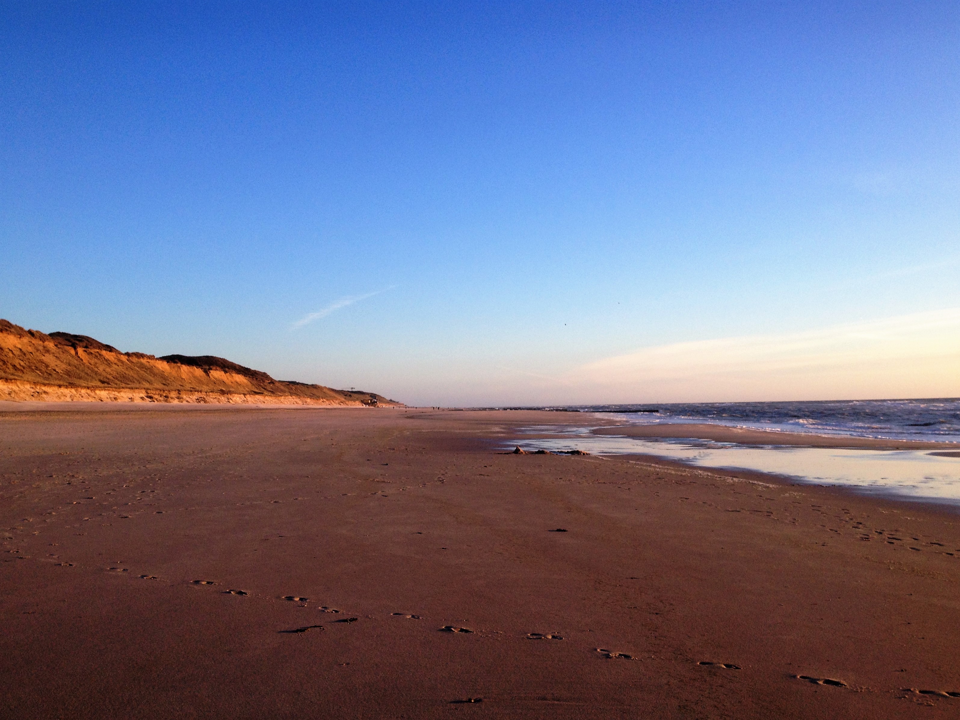 Reddish coastal cliff rising above a sandy beach along the North Sea coast of Sylt, Germany