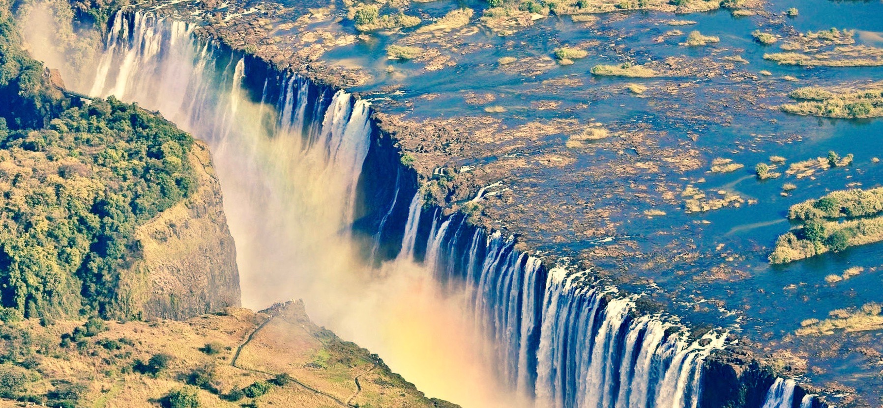 A sweeping 2017 photograph of Victoria Falls on the Zambezi River, showing the broad waterfall and gorge between Zambia and Zimbabwe.